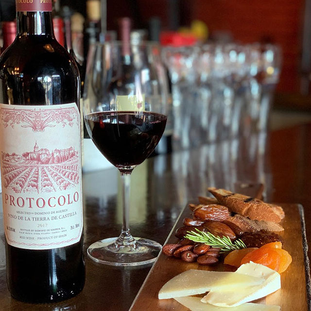 A bottle of red wine alongside a plate of cheese and fruit.